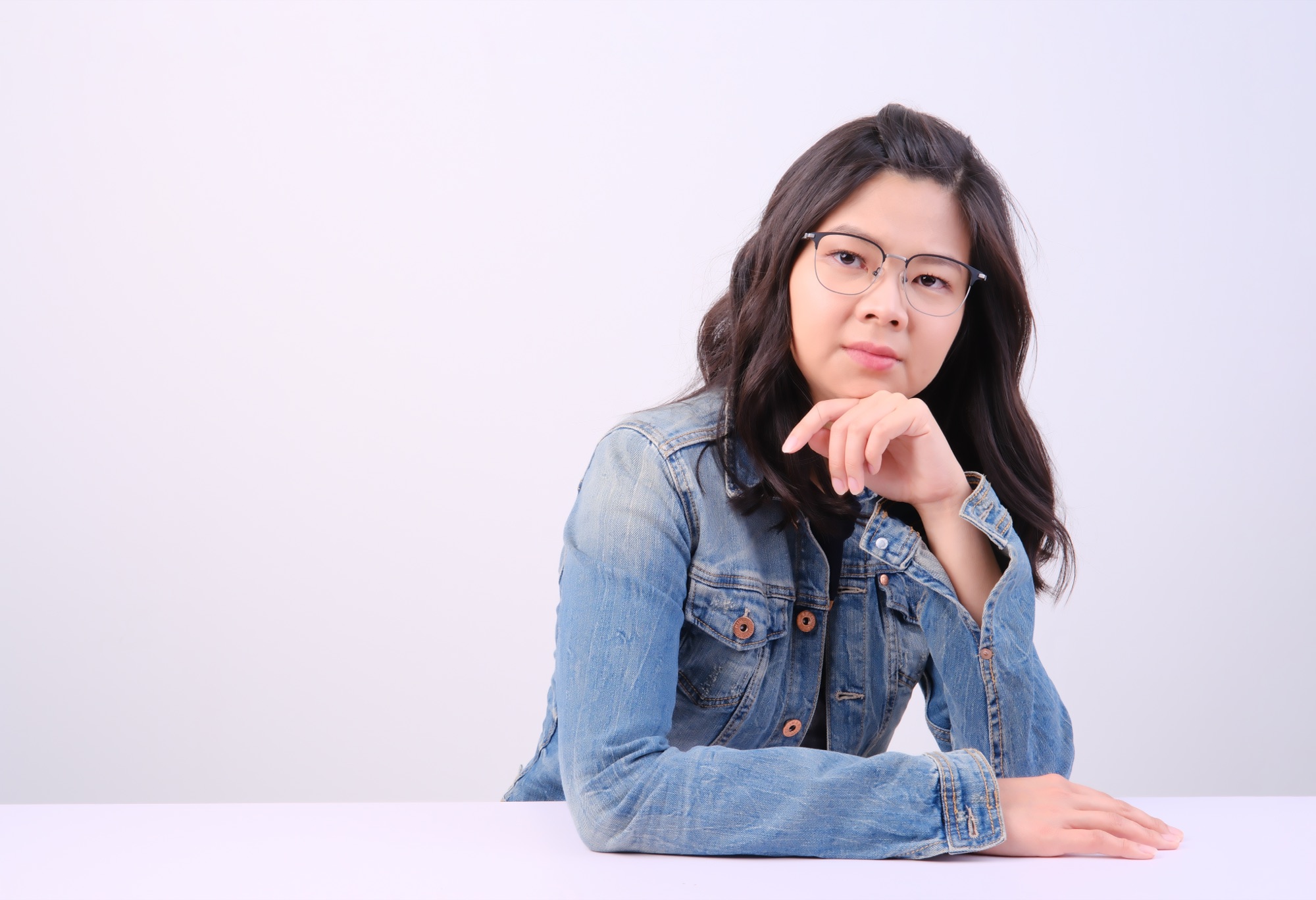 Jia Lin Cheoh seated at a table in a denim jacket, chin resting on her hand.